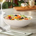 A bowl of salad with olives, grapes, and other vegetables in an Acopa Highlands white china bowl on a table.