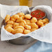 Breaded Tillamook Cheddar Cheese Curds in a bowl with red sauce and green onions.