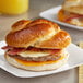 A Grand Prairie sausage, bacon, and cheese pretzel bun breakfast sandwich on a white plate.