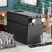 A black Fetco DRNX by BROOD DUO dual tap nitro cold brew beverage dispenser on a counter with glasses.