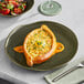 An Acopa Highlands Juniper Green coupe plate with a salad and a wine glass on a table.