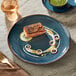 An Acopa Highlands blue china plate with a piece of salmon and a fork on a table.