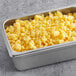 A metal container of Grand Prairie Frozen Fully Cooked Scrambled Eggs on a table in a school kitchen.