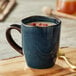 A blue Acopa Highlands china mug filled with a liquid on a table with a spoon and flower.