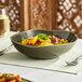 A bowl of salad with vegetables in an Acopa Highlands juniper green china bowl.