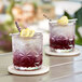 Two glasses of lavender Tiki Energy drink with lemon and lime on a table.