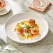 An Acopa Highlands white coupe plate on a table with food and a glass of wine.