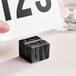A hand holding a card over an American Metalcraft black marble cube with a card in it.