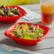 A salad in a Solo Squared red plastic bowl on a table in a salad bar.