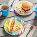 A table with Solo AnyDay paper plates, a cheeseburger, a hot dog, a blue cup, and brown liquid.