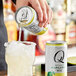 A person pouring Q Mixers Premium Margarita mix from a can into a glass with ice.