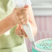 A person using a clear disposable pastry bag to decorate a cake with white icing.