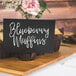 A tray of blueberry muffins with a white sign on it that says "blueberry muffins" on a table.