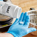 A hand in blue gloves holding a Bunn coffee cleaning tablet.