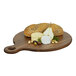 A Cal-Mil walnut round serving board with cheese and bread on a table.