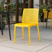 A Lancaster Table & Seating Rio Sunshine Yellow resin side chair on an outdoor patio.