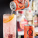 A hand pours Q Mixers Sparkling Grapefruit from a can into a glass with a slice of orange.