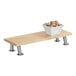 A Cal-Mil maple rectangle display stand with stainless steel legs holding a bowl of brown food on a wooden table.