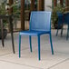 A blue plastic Lancaster Table & Seating Rio side chair on an outdoor patio.