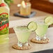 A glass of Jose Cuervo margarita mix with a lime slice next to a bottle.