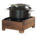 A black pot with silver handles and lid sits on a walnut wood countertop induction range with a digital control panel.