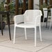 A white Lancaster Table & Seating Rio resin arm chair at a table on a patio.