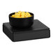 A black Cal-Mil cube display stand holding a bowl of pineapple chunks.