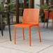 A Lancaster Table & Seating Rio Sunset Orange resin side chair on an outdoor patio.