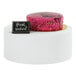 A white metal round display stand with a pink cake on top.