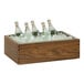 A Cal-Mil walnut ice housing with clear pan holding bottles of water on a table.