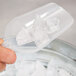 A hand holding a Fineline clear utility scoop of ice over a clear plastic cup.