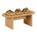 A Cal-Mil faux wood oval display stand on a table with food on it.