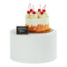 A cake with whipped cream and cherries on a Cal-Mil white metal display stand.