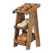 A Cal-Mil walnut wood 3-tier display merchandiser with bread on each shelf.