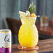 A glass of Q Mixers Tropical Ginger Beer with yellow liquid and fruit on a table.