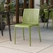 A Lancaster Table & Seating Rio Sea Moss Green resin side chair on an outdoor patio.