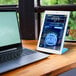 A white tablet with blue text next to a laptop on a wooden table.