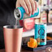 A hand pouring Q Mixers Premium Club Soda from a blue can into a cup.