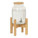 A Cal-Mil round glass beverage dispenser with a faux wood base and a faucet.