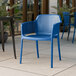 A blue plastic Lancaster Table & Seating Rio arm chair on an outdoor patio.