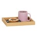 A faux wood Cal-Mil room service tray with a pink mug and pastry on it.