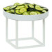 A white metal cube display riser with a bowl of sliced cucumbers on top.