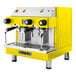 A yellow and silver Astra Mega II compact espresso machine with two coffee cups.