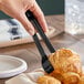 A pair of 7-inch black plastic tongs being used to pick up a croissant.