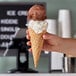 A hand holding a JOY large waffle cone with chocolate and vanilla ice cream.