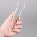 A hand holding a pair of clear plastic tongs.