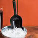 A black Fineline utility and ice scoop in a bowl of ice cubes.