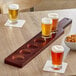 An Acopa mahogany beer flight paddle with glasses of beer and pretzels on a table.