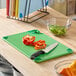 A set of color-coded cutting boards with a green board in use, featuring a knife and sliced bell peppers on a kitchen counter.