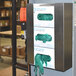 A stainless steel Omnimed disposable glove dispenser with three green glove boxes on a counter.